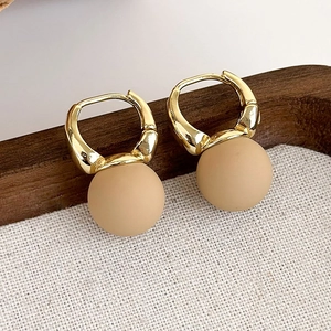 Dettaglio di orecchini a cerchio geometrici con perline beige opache su vassoio in legno