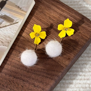 Detail of yellow flower earrings with white fur pom-poms on a rustic wooden tray