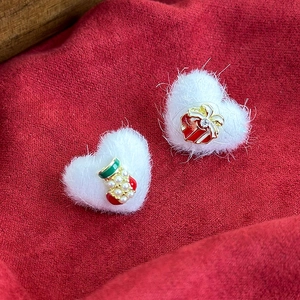 Close-up of white plush heart earrings with Christmas stocking and red gift box charms