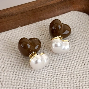 Primo piano di orecchini vintage a cuore in marrone e bianco perla su tessuto beige