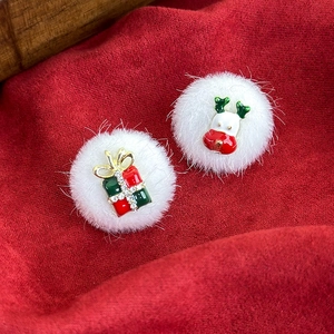 Close-up of asymmetric Christmas stud earrings with white faux fur balls and festive charms