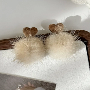 Close-up of fluffy beige faux fur earrings with brown corduroy heart detail on a tray