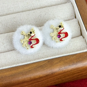Macro shot of white plush earrings with gold Fu character and festive red enamel details