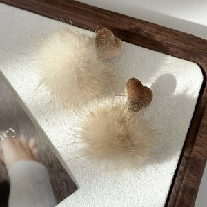 Detail view of heart-shaped earrings with plush fur balls in warm beige and brown tones