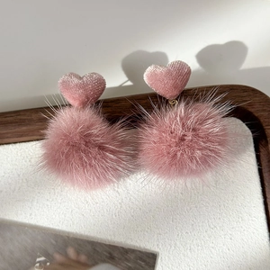 Detail of pink faux mink fur ball earrings with textured heart stud and soft shadows