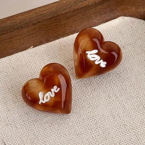 Dettaglio di orecchini a cuore in resina marrone caffè con texture ambra e scritta love