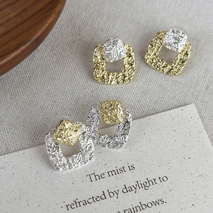 Macro detail of square metal stud earrings with textured relief and mixed metal finish