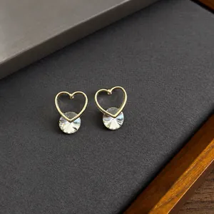 Minimalist gold heart stud earrings with round zircon stones on a gray display card