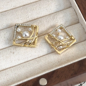 Detailed view of geometric gold square earrings with pearls and pavé zircons in a box