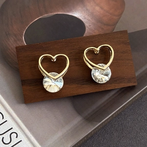 Detailed view of heart-shaped gold earrings with large clear zircon on a wooden stand
