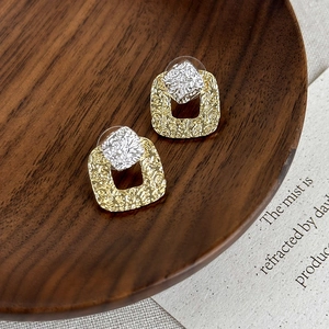 Detailed view of bicolor irregular texture metal square earrings on a dark wood tray