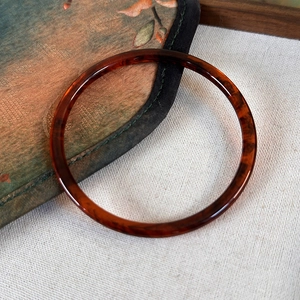 Close-up of amber tortoiseshell resin bangle on vintage linen with oil painting pouch