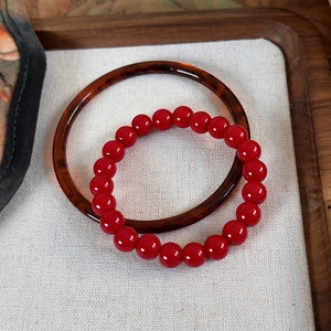 Red beaded bracelet with amber texture bangle set on a wooden tray background