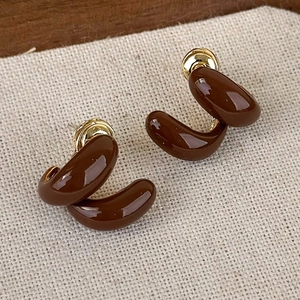 Dettaglio di orecchini vintage geometrici smaltati marroni su fondo di lino beige
