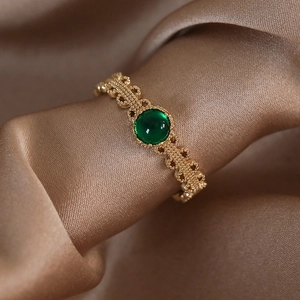 Dettaglio macro di un anello in pizzo dorato retrò con gemma rotonda verde smeraldo