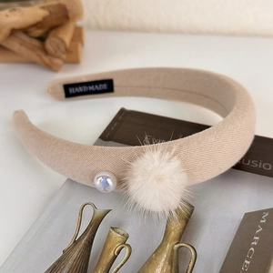 Detail eines handgefertigten Strickstirnbands mit weißer Perle und flauschigem Bommel