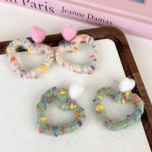 Detailed close-up of rainbow heart-shaped yarn earrings with colorful plush velvet pom-poms