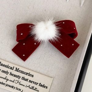 Détail d'une pince à cheveux nœud en velours rouge avec pompon blanc et strass argentés