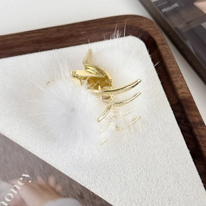 Détail d'une pince à cheveux dorée avec pompons en fourrure blanche sur plateau bois