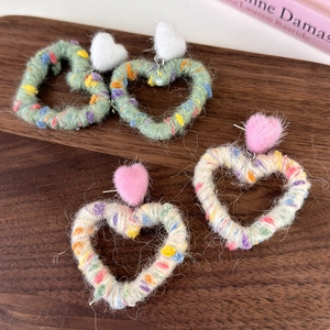 Detailed close-up of rainbow knit heart earrings with fuzzy pom poms on a wooden tray