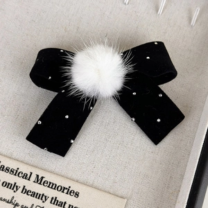 Vue détaillée d'une barrette noeud en velours noir avec pompon en fourrure et faux diamants
