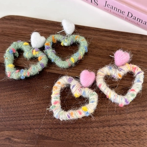 Macro detail of rainbow yarn heart earrings with soft plush pompoms on a wooden surface
