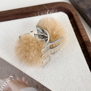 Détail de pompons en peluche beige sur une pince à cheveux en métal argenté