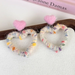 Detail of handmade rainbow yarn-wrapped heart earrings with soft pink plush studs