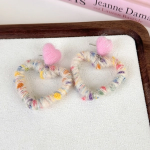 Detailed macro view of colorful wool-wrapped heart earrings with pink plush ball accents