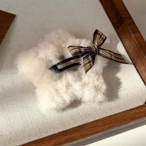 Close-up of plush star hair clip with brown plaid bow on a cozy wooden tray