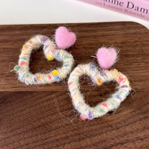 Detailed macro of handmade rainbow yarn-wrapped heart earrings on wooden surface