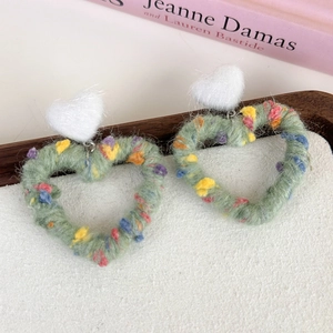 Close-up of rainbow knit heart earrings with green wool and white plush tops