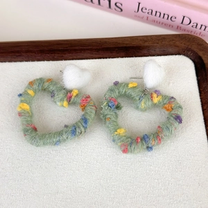 Close-up of green yarn-wrapped heart earrings with colorful speckles and plush tops