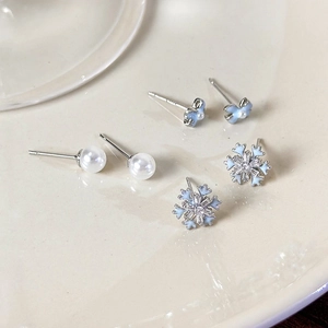 Macro shot of pearl earrings with bow and snowflake designs on white ceramic
