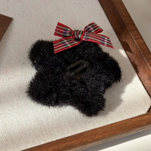 Close-up of black plush star hair clip with a red tartan bow on a rustic display