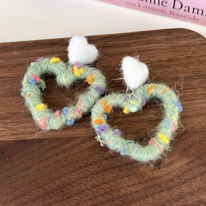 Close-up of heart-shaped knit earrings with light green yarn and colorful fiber speckles