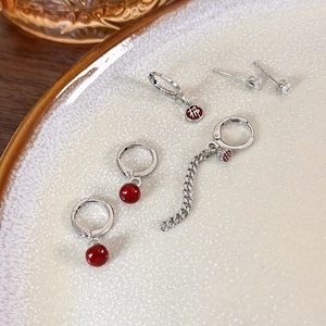 Detail of New Year silver earrings set with red charms and crystals on beige tray