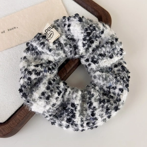 Detail of checkered plush scrunchie with woven label in a wooden tray background