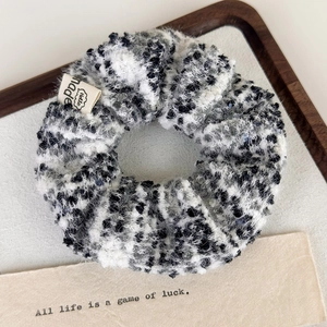 Detail of plush tweed scrunchie in black and white with a minimalist beige fabric label