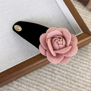 Detail of pink velvet camellia hair clip with gold metal accent on a textured tray