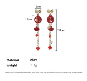 Détail des boucles d'oreilles éventail rouge avec nœud doré et perles de fête