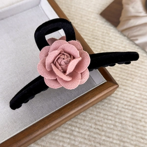 Detail of pink fabric camellia flower on a black velvet hair claw clip on a tray
