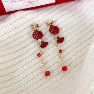Détail de boucles d'oreilles à pompon rouge avec éventail Fu doré et perles sur tricot