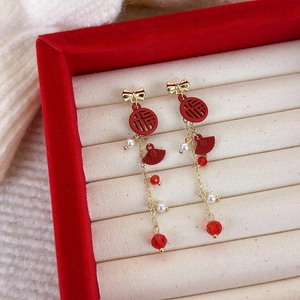 Détail de boucles d'oreilles rouges avec signe Fu, nœud doré et pompons en perles blanches