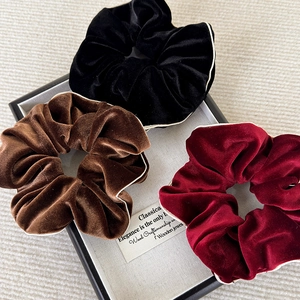 Détail de chouchous en velours noir, marron et bordeaux avec bordure contrastée