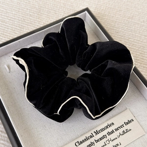 Détail d'un chouchou en velours noir avec surpiqûre blanche dans son coffret