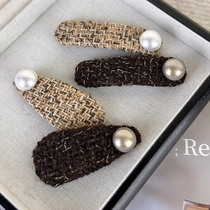 Detailed view of tweed fabric hair clips set with large pearl accents in brown tones