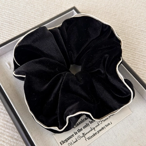 Gros plan d'un chouchou en velours noir avec liseré blanc dans un coffret cadeau