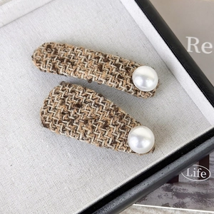 Close-up of brown tweed fabric texture and white pearl detail on elegant hair clips