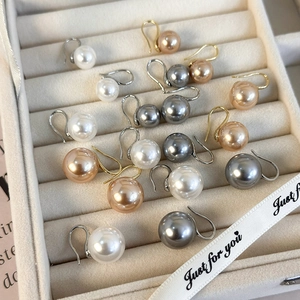 Detalle de pendientes de perlas grises y doradas en un joyero de terciopelo color beige